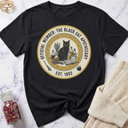 Black t-shirt with a black cat and apothecary design on a marble surface.