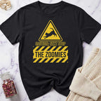 Black t-shirt with yellow warning sign graphic and text 'Caution: Next Stop The Zoomies' on a marble surface.