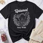 Black t-shirt with a cat graphic and text 'Untamed Stay Wild' on a marble surface.