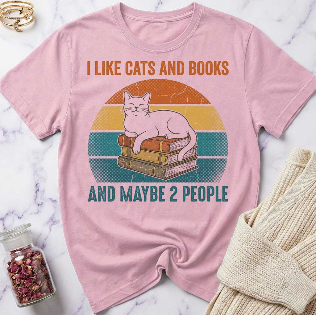 Pink t-shirt with a cat and books graphic and text on a marble surface.