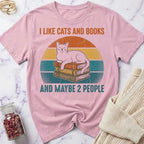 Pink t-shirt with a cat and books graphic and text on a marble surface.