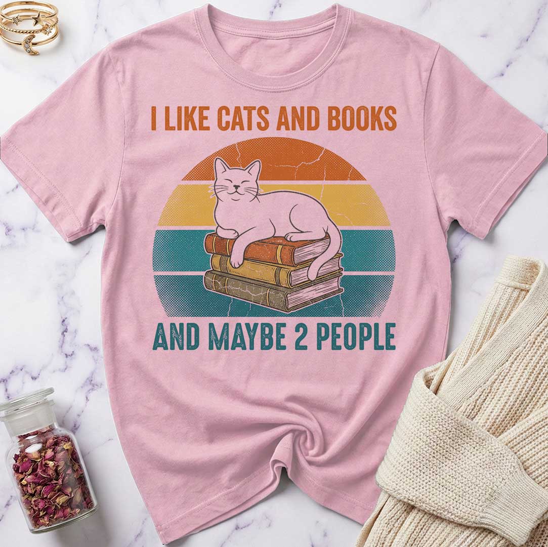 Pink t-shirt with a cat and books graphic and text on a marble surface.