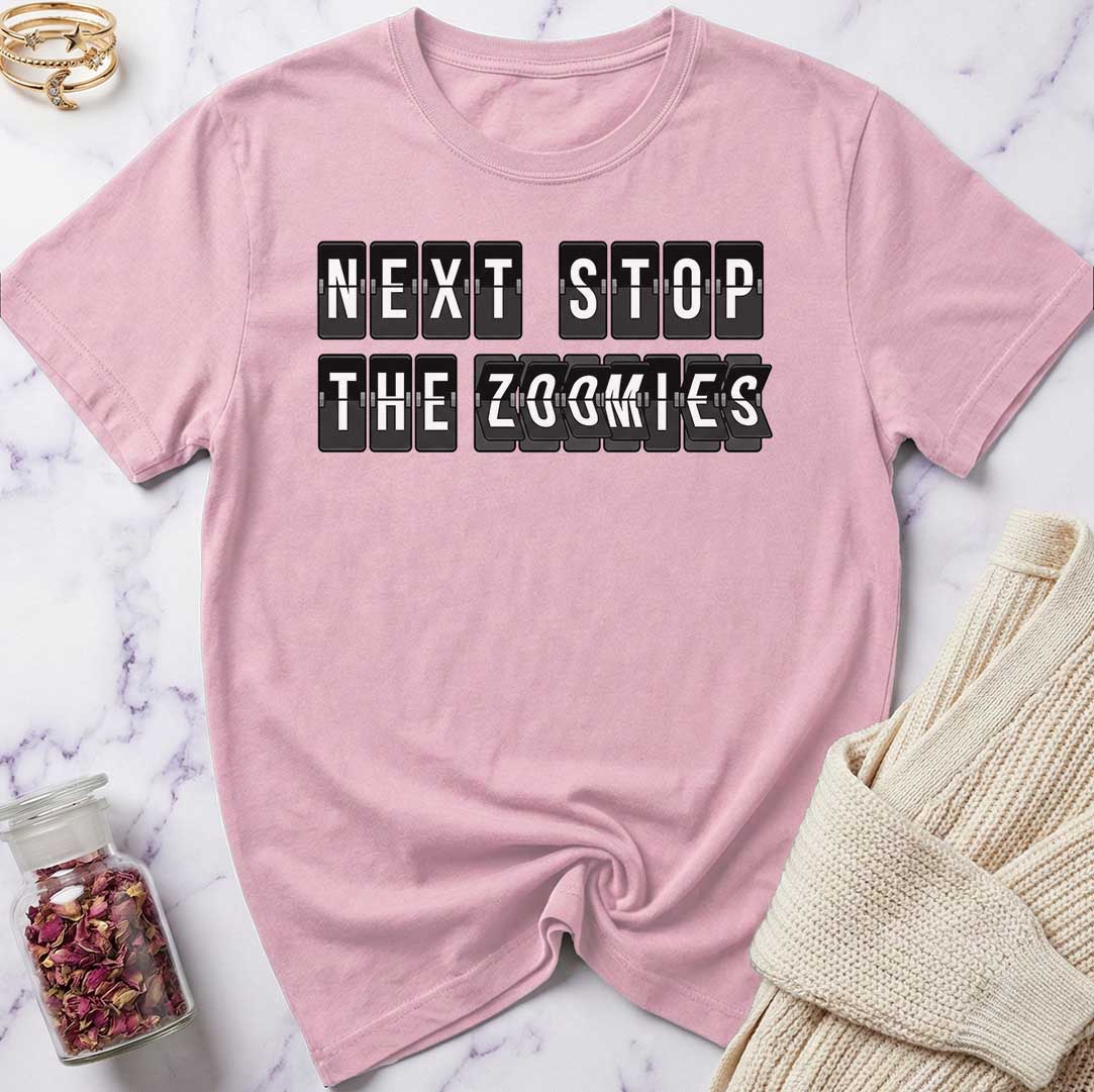 Pink t-shirt with 'Next Stop The Zoomies' text on a marble surface.