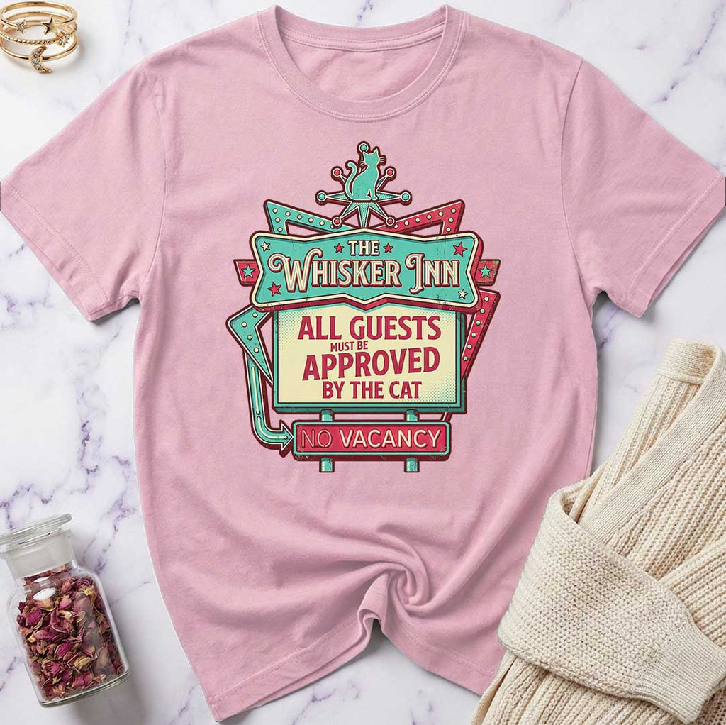 Pink t-shirt with 'The Whisker Inn' graphic design on a marble surface.