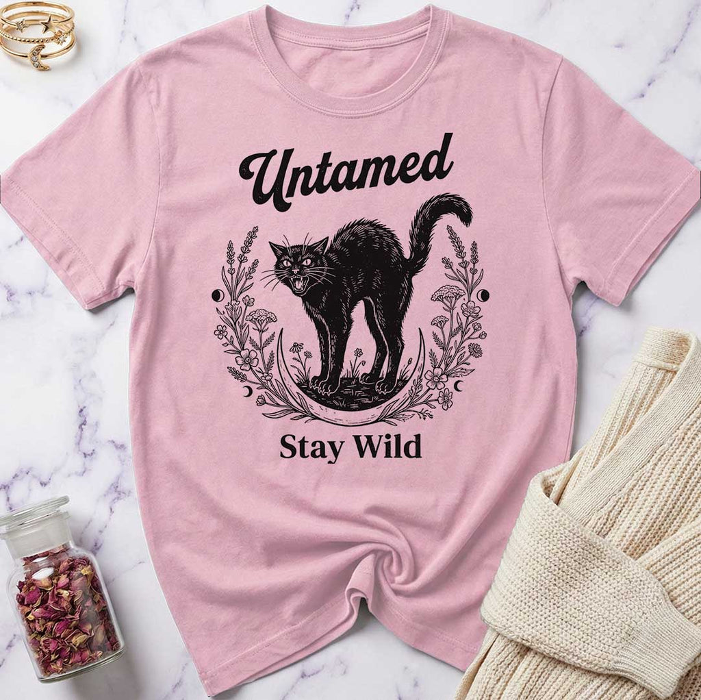 Pink t-shirt with black cat graphic and text 'Untamed Stay Wild' on a marble surface.