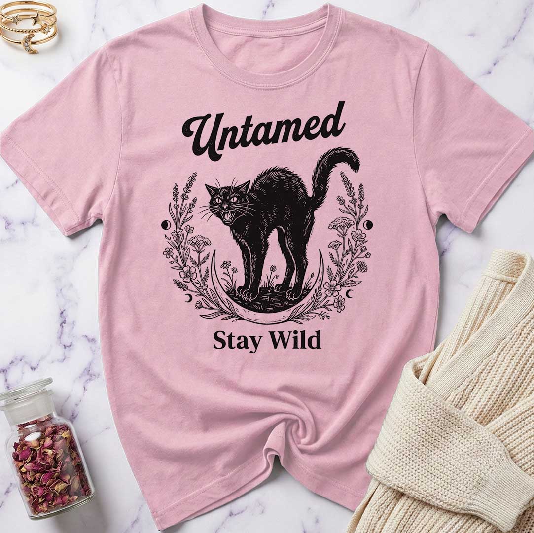 Pink t-shirt with black cat graphic and text 'Untamed Stay Wild' on a marble surface.