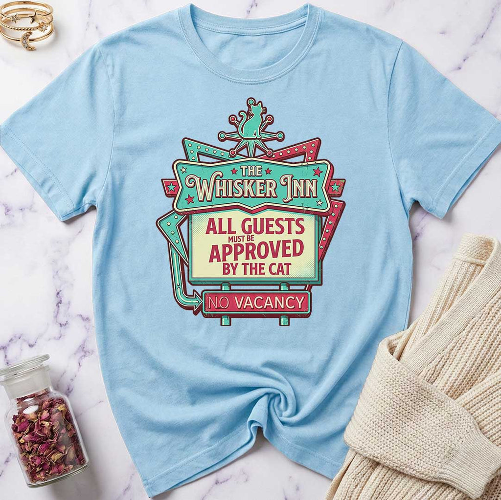 Light blue t-shirt with 'The Whisker Inn' graphic design on a marble surface.