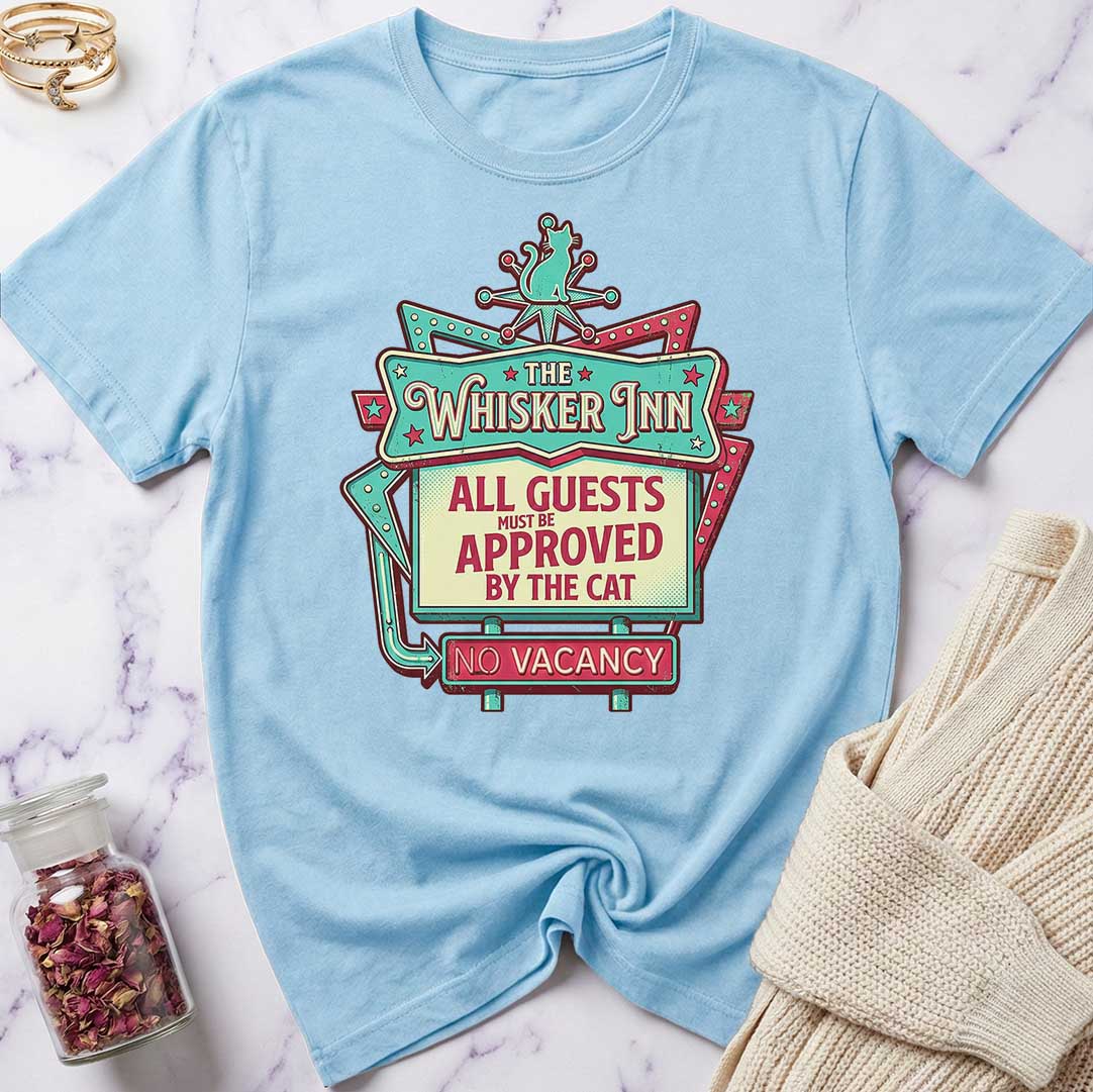 Light blue t-shirt with 'The Whisker Inn' graphic design on a marble surface.