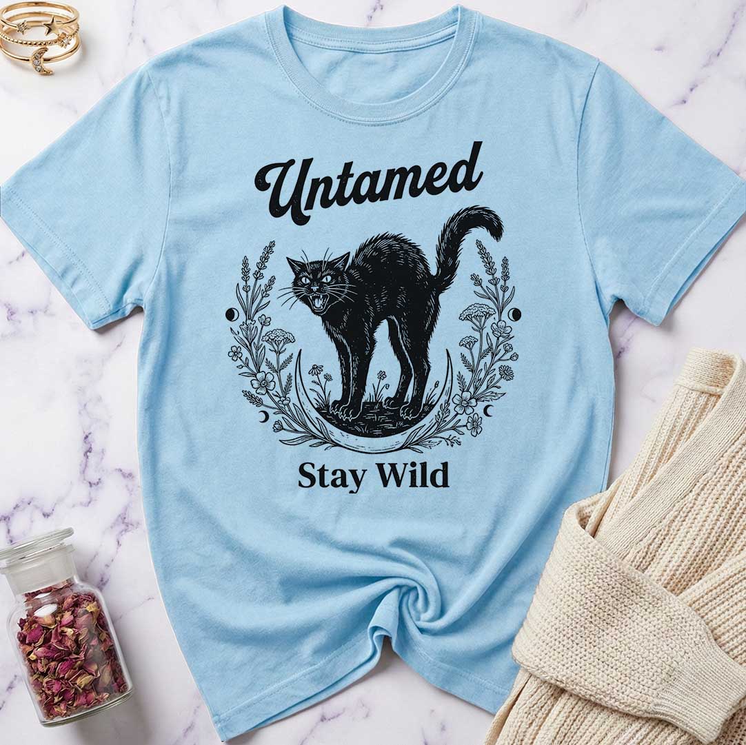Light blue t-shirt with black cat graphic and text 'Untamed Stay Wild' on a marble surface.