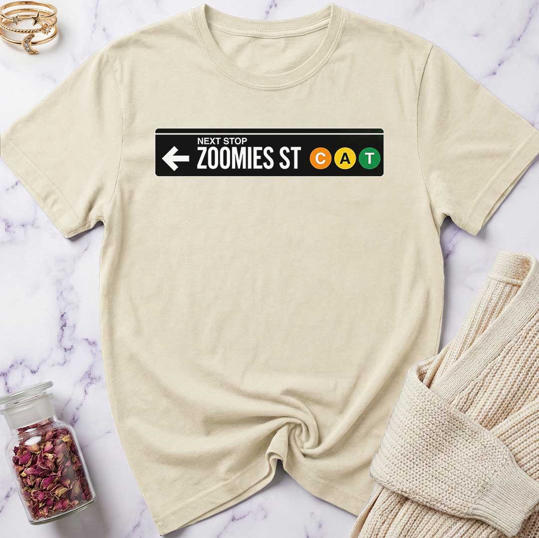 Beige t-shirt with a 'Next Stop Zoomies St CAT' graphic on a marble surface.
