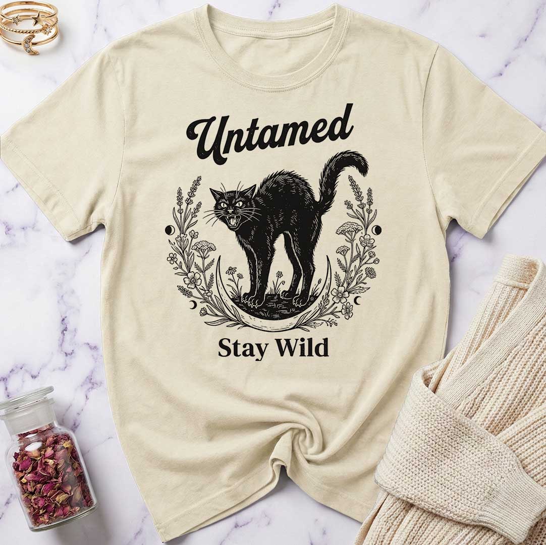 Beige t-shirt with black cat graphic and text 'Untamed Stay Wild' on a marble surface.