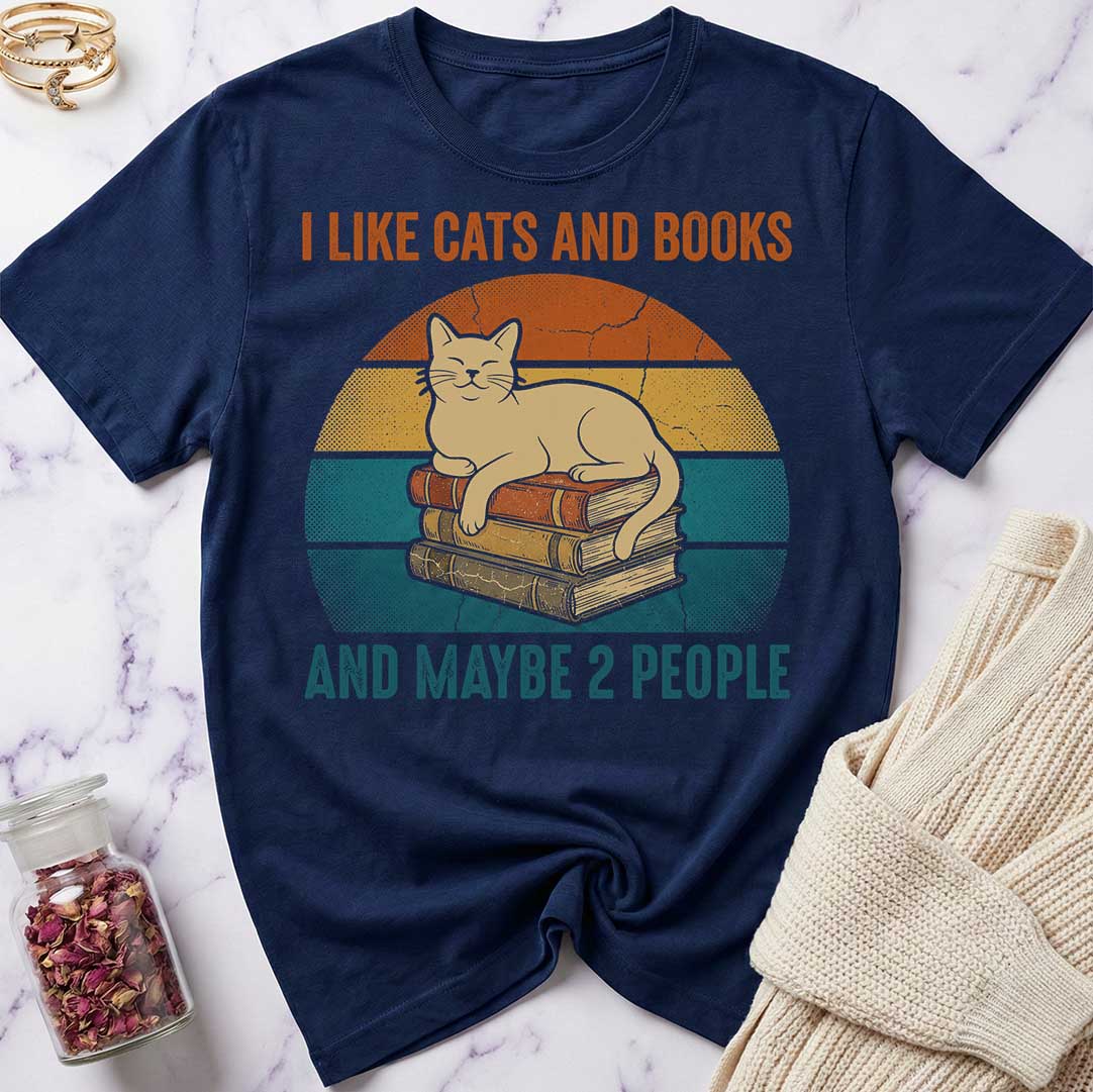 Navy blue t-shirt with a graphic of a cat on books and text 'I like cats and books and maybe 2 people' on a marble surface.