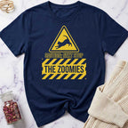 Navy blue t-shirt with yellow warning sign graphic and text 'Caution: Next Stop The Zoomies' on a marble surface.