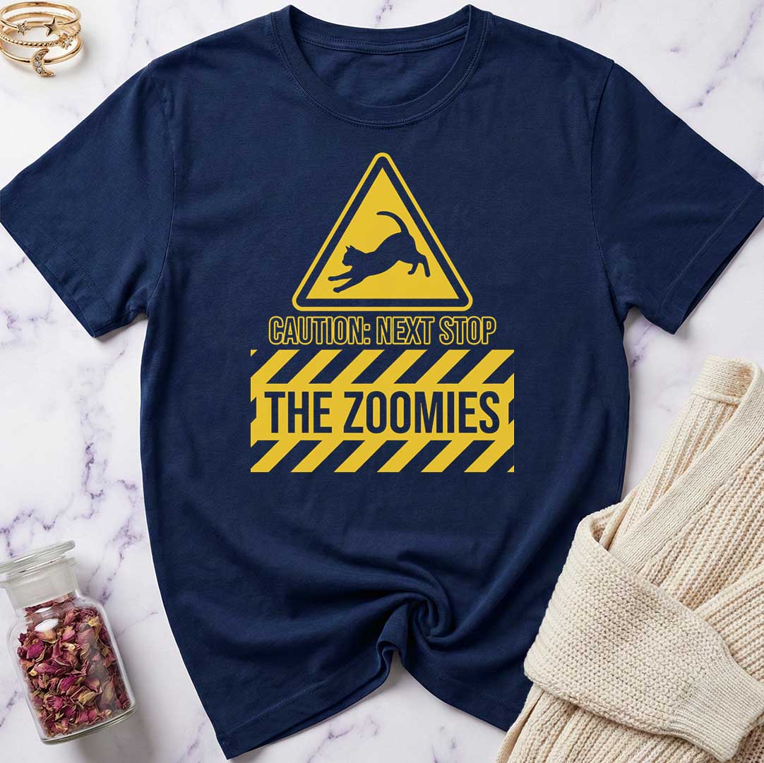 Navy blue t-shirt with yellow warning sign graphic and text 'Caution: Next Stop The Zoomies' on a marble surface.