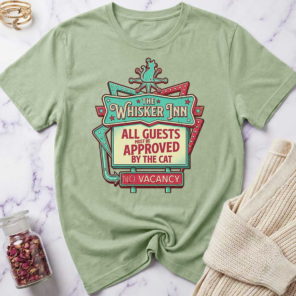 Green t-shirt with 'The Whisker Inn' graphic design on a marble surface.
