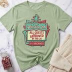 Green t-shirt with 'The Whisker Inn' graphic design on a marble surface.