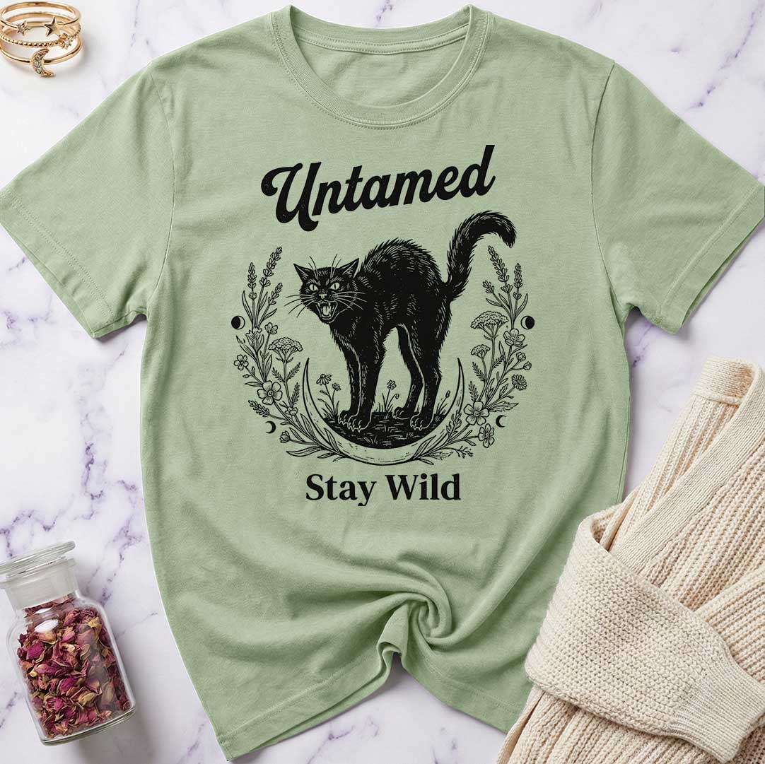Green t-shirt with black cat graphic and text 'Untamed Stay Wild' on a marble surface.