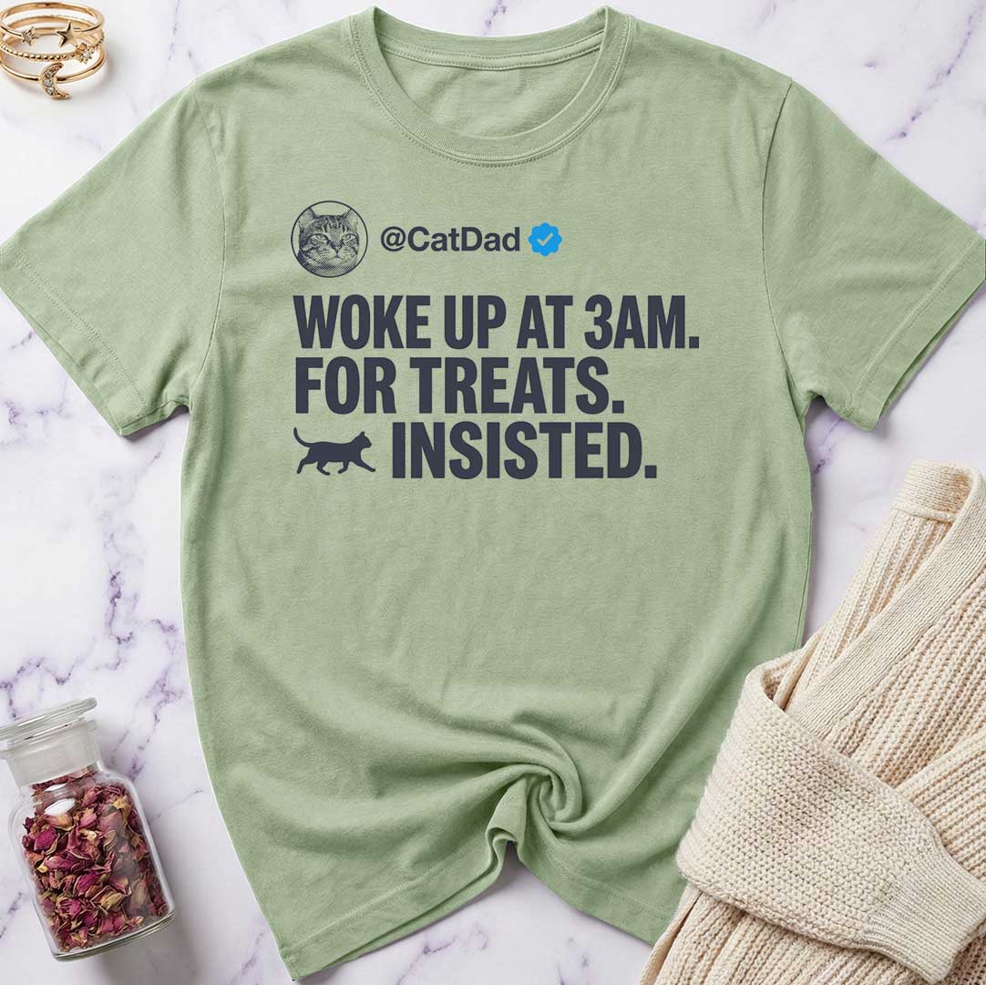 Green t-shirt with text 'Woke up at 3AM. For treats. Insisted.' on a marble surface.
