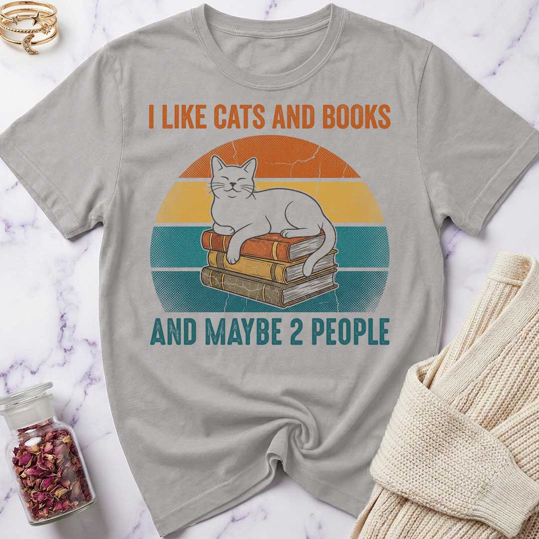 Gray t-shirt with a graphic of a cat on books and text 'I like cats and books and maybe 2 people' on a marble surface.