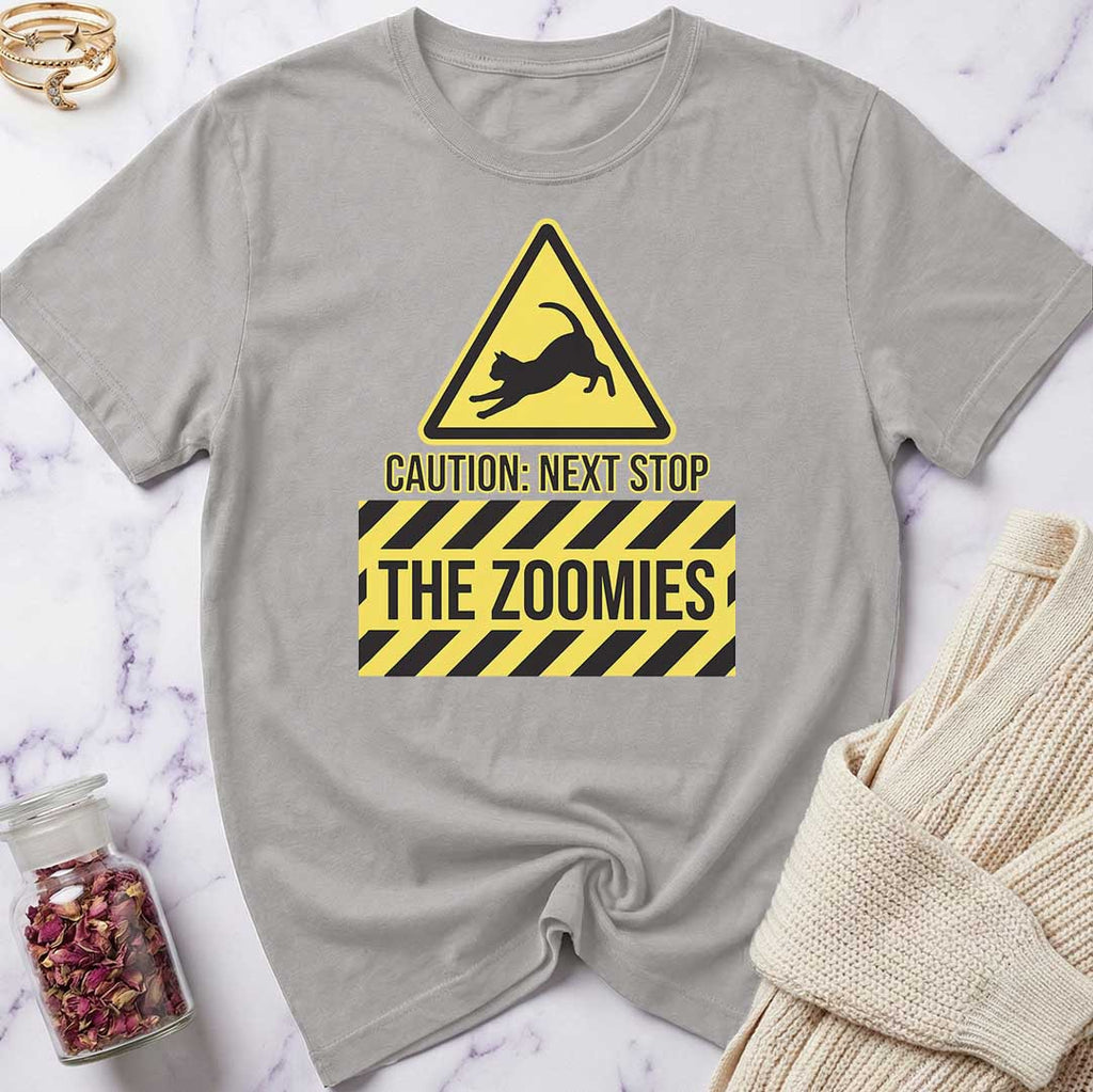 Gray t-shirt with a yellow and black warning sign graphic and text 'CAUTION: NEXT STOP THE ZOOMIES' on a marble surface.