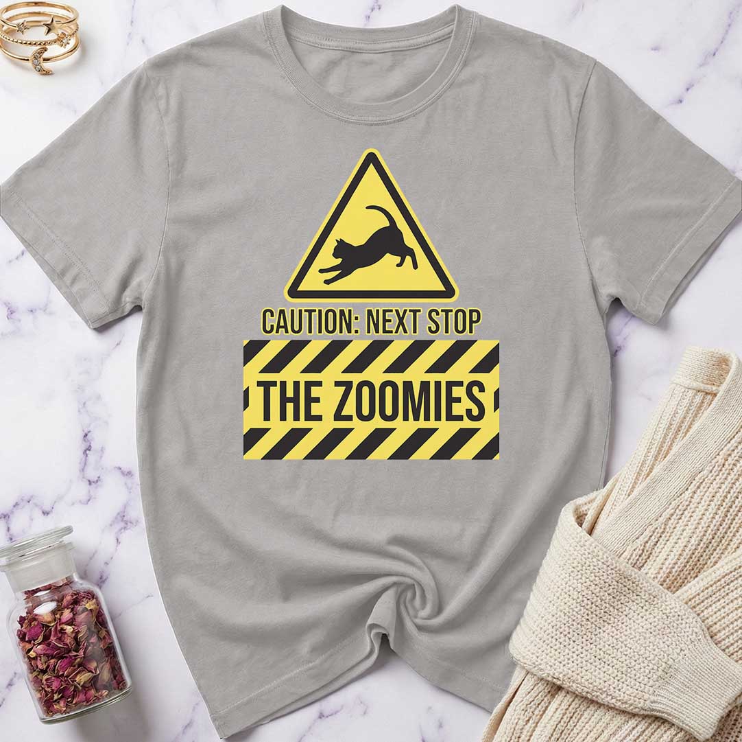 Gray t-shirt with a yellow and black warning sign graphic and text 'CAUTION: NEXT STOP THE ZOOMIES' on a marble surface.