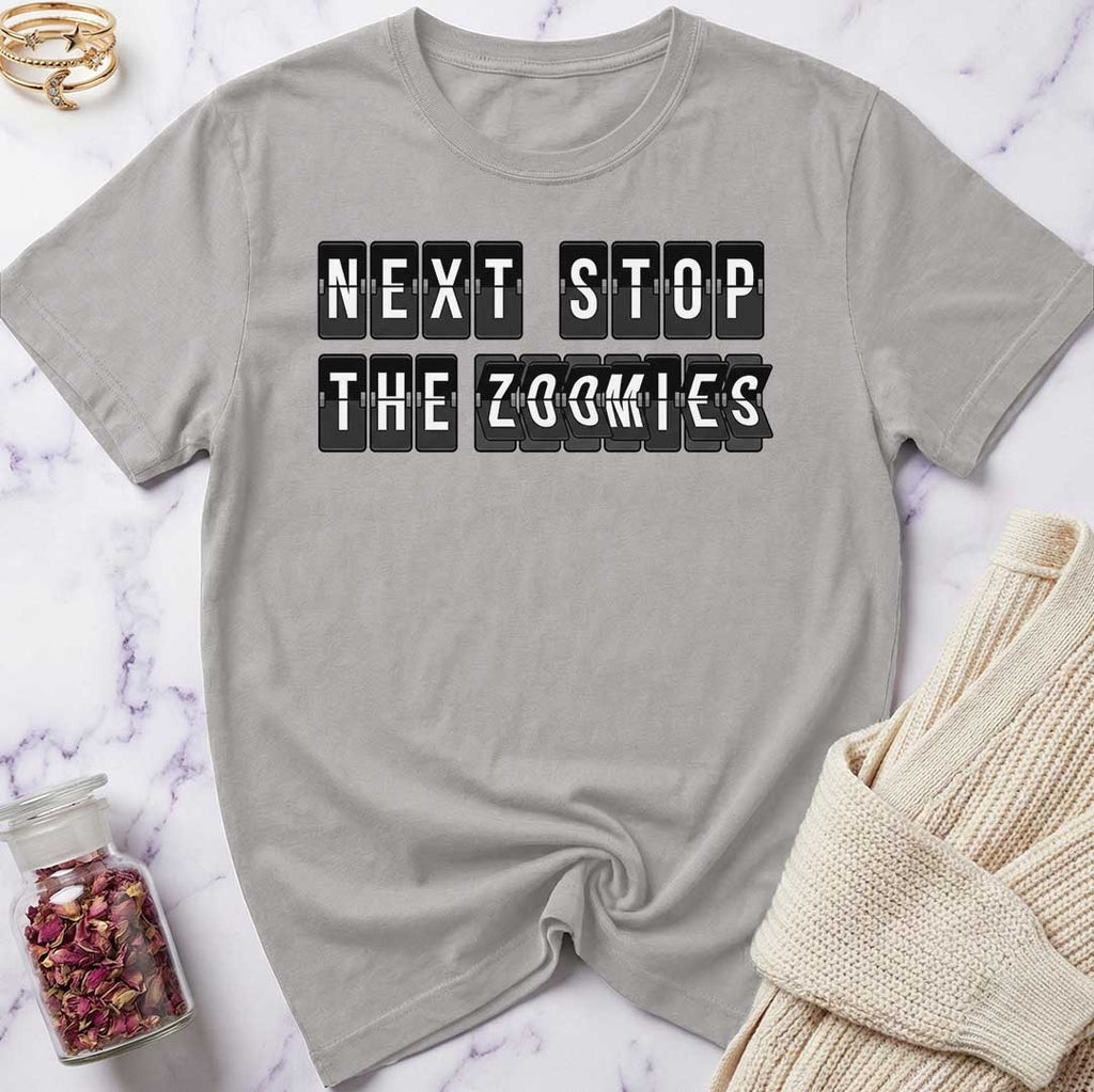 Gray t-shirt with 'Next Stop The Zoomies' text on a marble surface with a knit item and jar.
