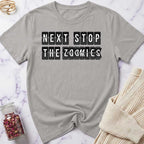 Gray t-shirt with 'Next Stop The Zoomies' text on a marble surface with a knit item and jar.