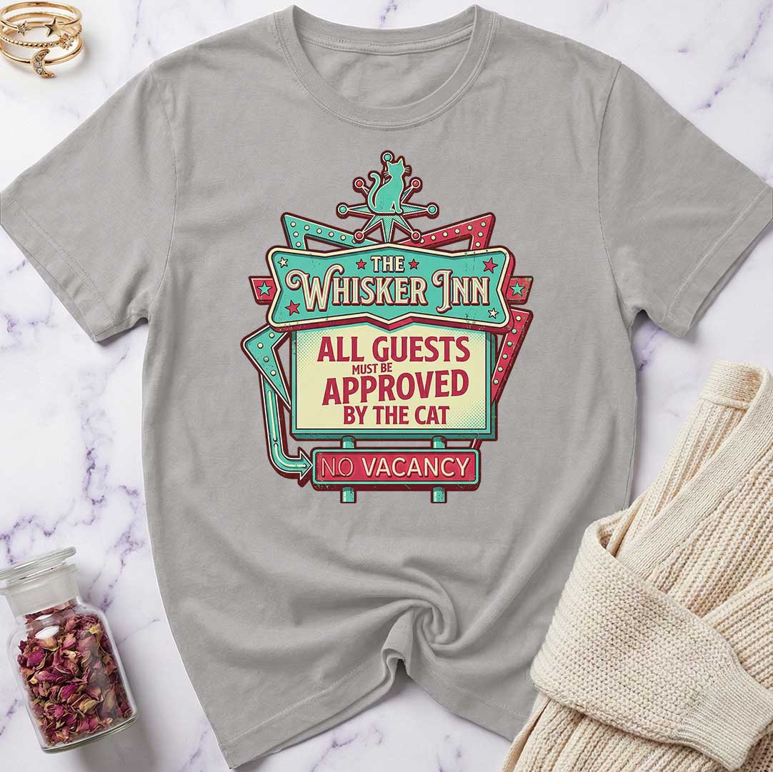 Gray t-shirt with 'The Whisker Inn' graphic design on a marble surface.