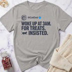 Gray t-shirt with humorous text design on a marble surface with a sweater and jar of treats.