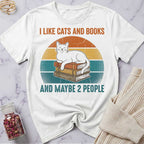 White t-shirt with a graphic of a cat on books and text 'I Like Cats and Books and Maybe 2 People' on a marble surface.