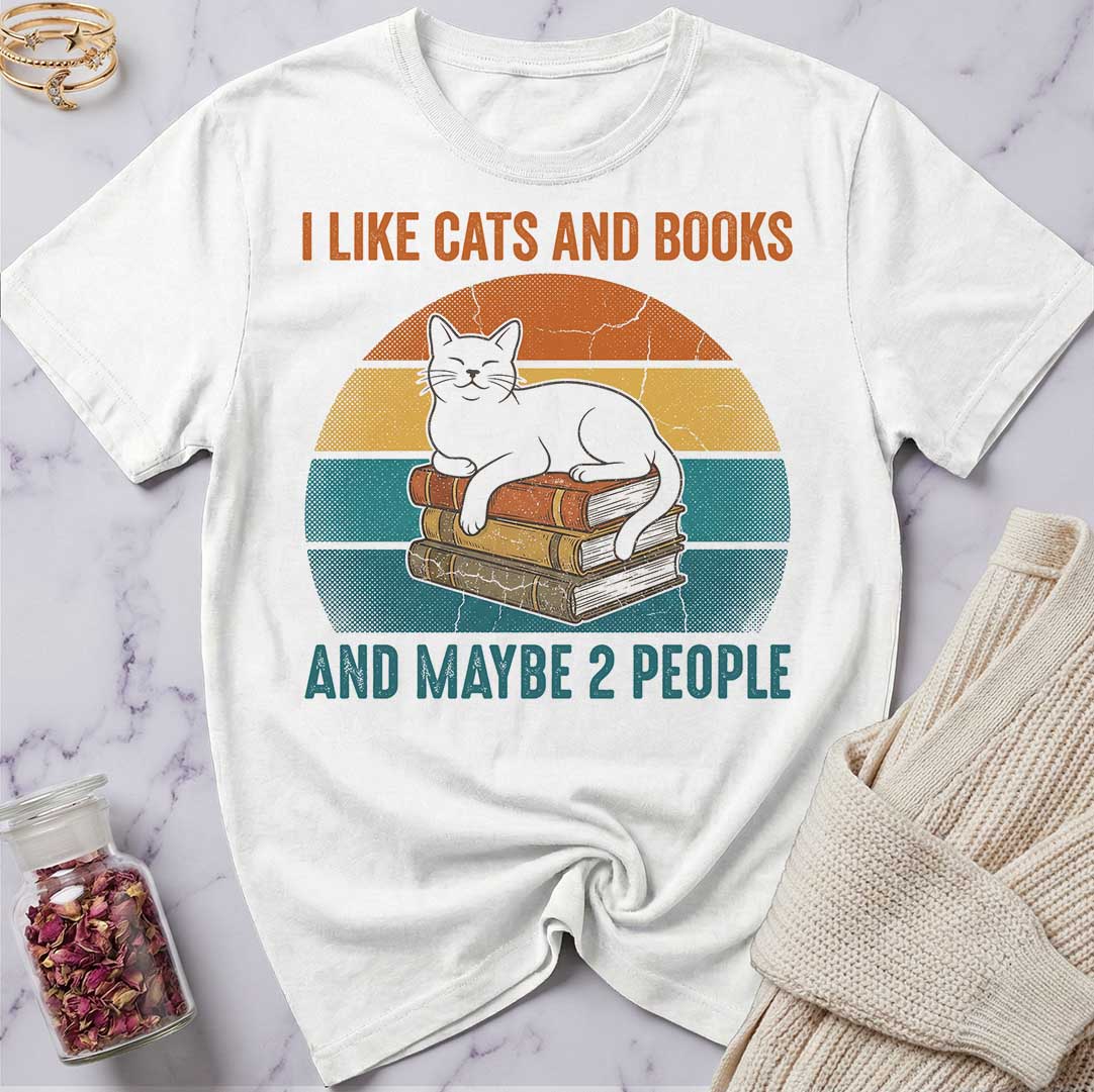 White t-shirt with a graphic of a cat on books and text 'I Like Cats and Books and Maybe 2 People' on a marble surface.