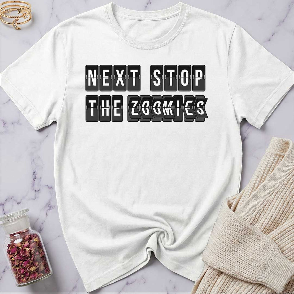 White t-shirt with 'Next Stop The Zoomies' text on a marble surface with a sweater and jar of rose petals.
