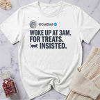 White t-shirt with humorous text design on a marble surface with a sweater and jar of dried flowers.