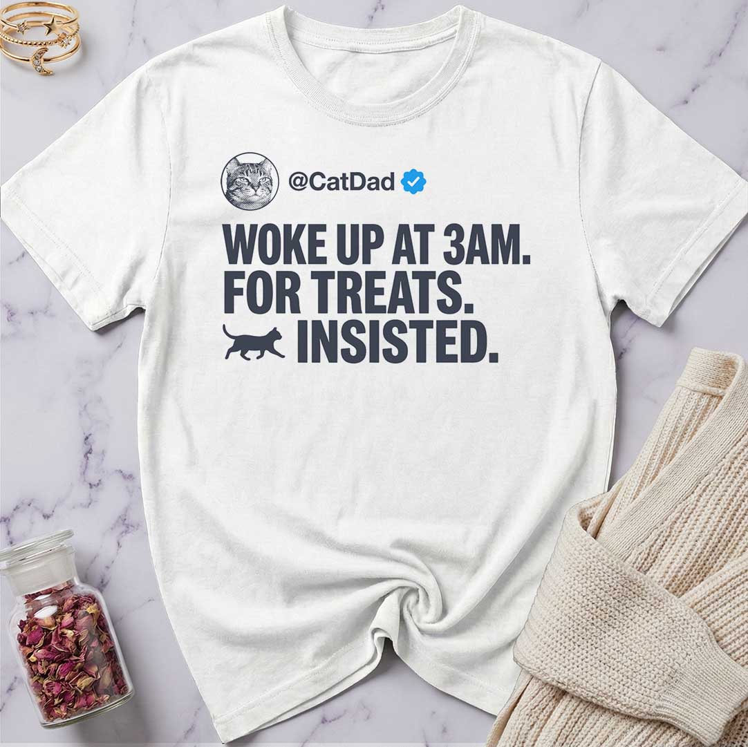 White t-shirt with humorous text design on a marble surface with a sweater and jar of dried flowers.